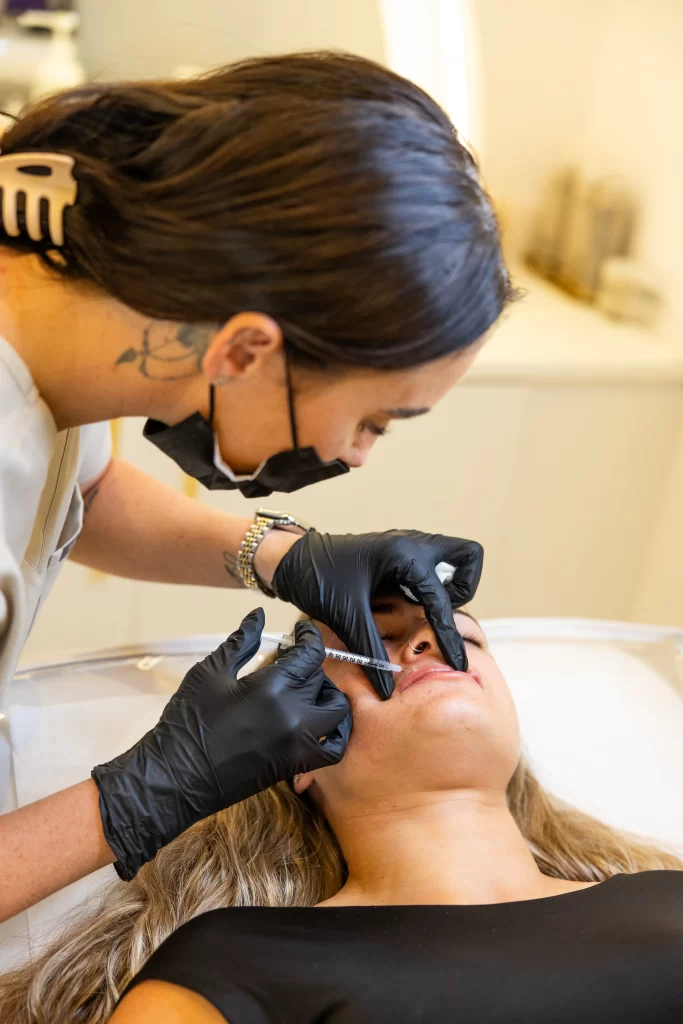 A beauty technician injecting a clients lips with a dermal filler